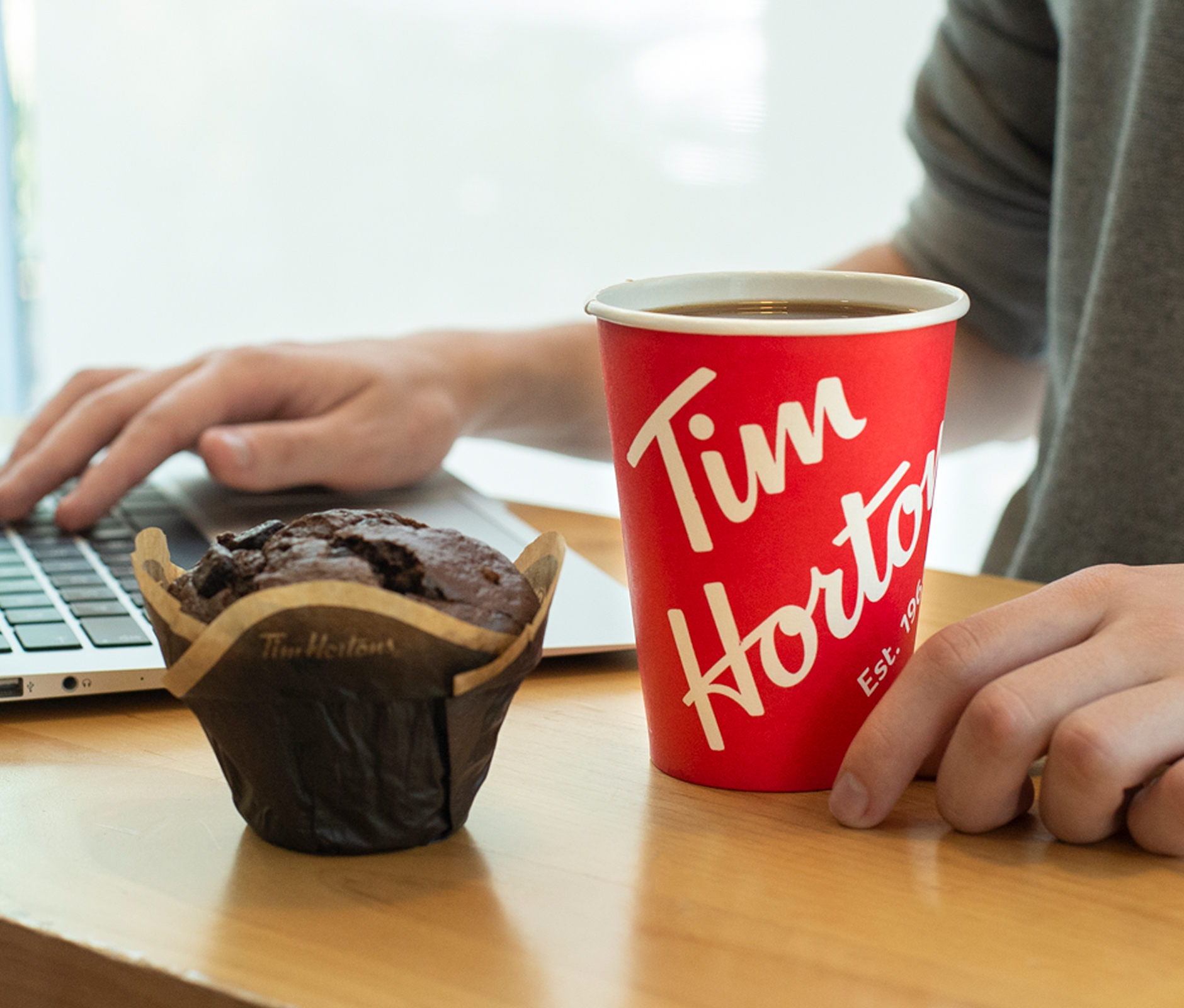 Man using his computer and enjoying a cup of coffee and muffin from Tim Hortons