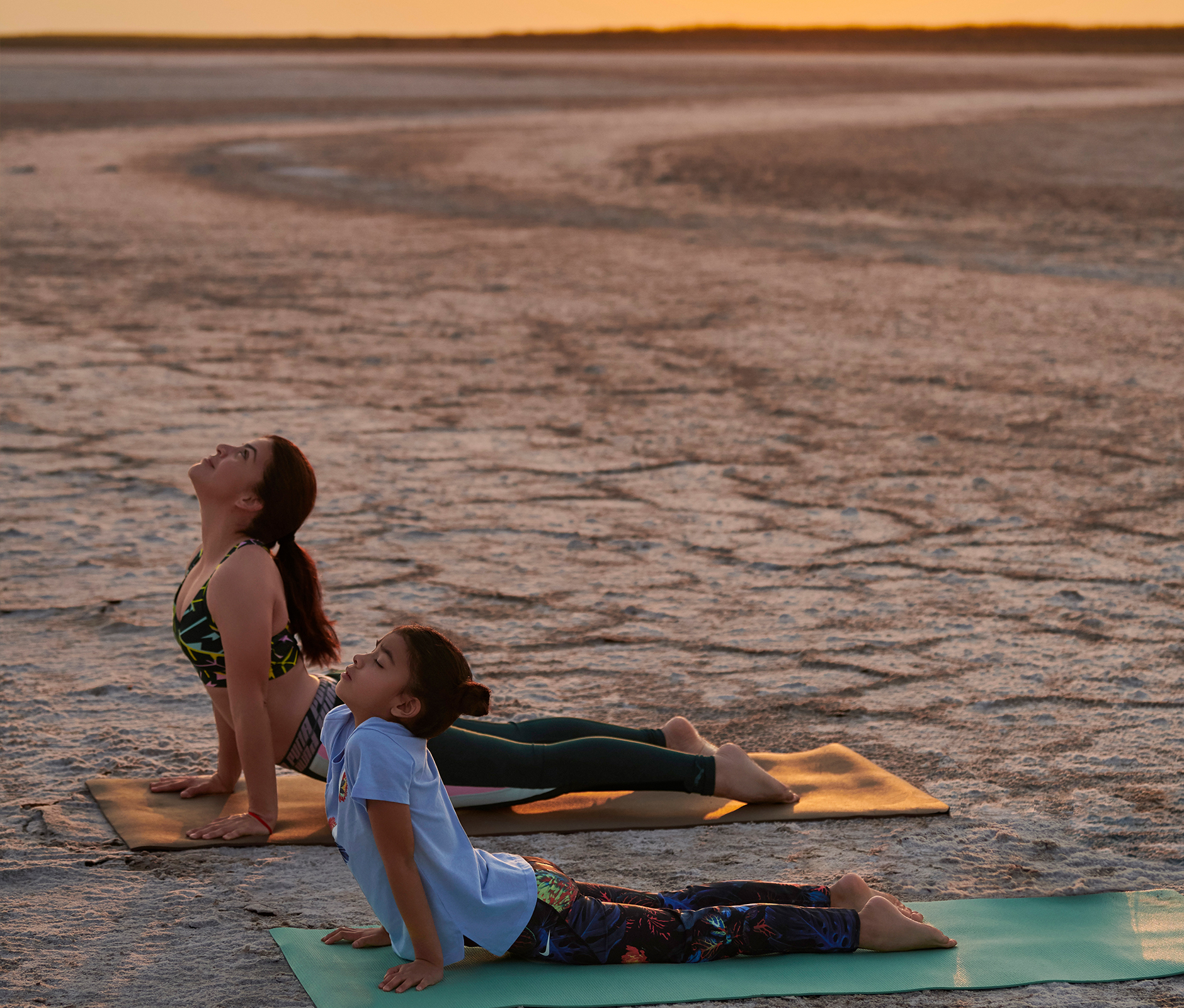 Mom and daughter practising bhujangasana yoga pose at desert